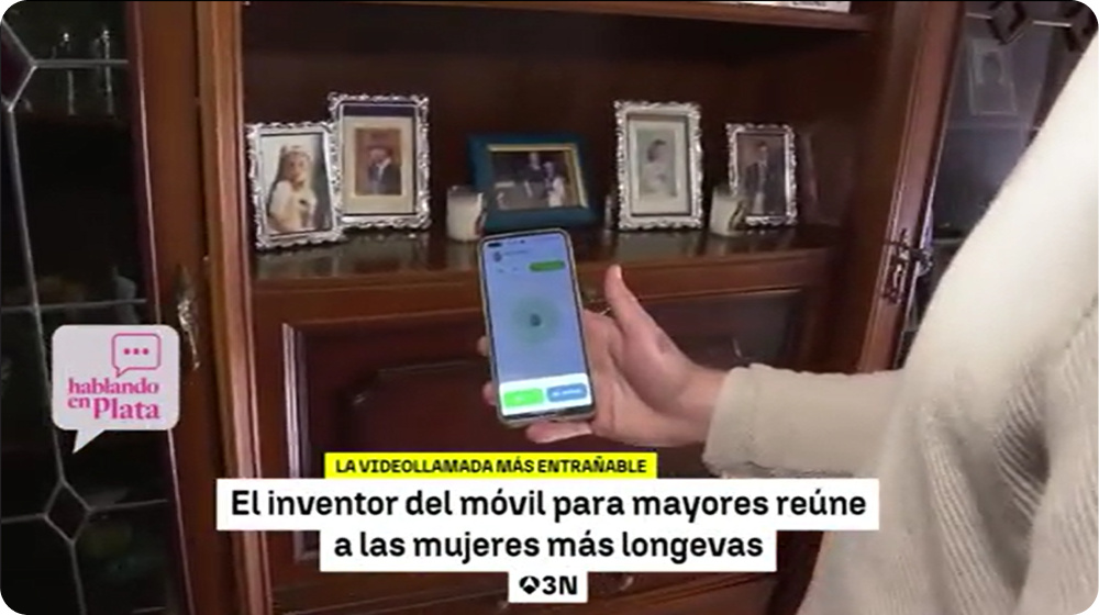 Persona mayor con un móvil en la mano haciendo una videollamada, junto al texto "El inventor del móvil para mayores reúne a las mujeres más longevas".